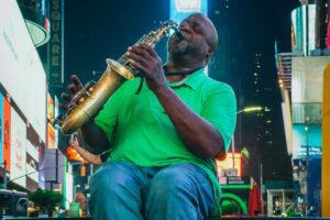 En la imagen, un músico vestido con una camisa verde y jeans toca el saxo en lo que parece ser una calle bulliciosa, quizás en un gran centro urbano. Las luces de los letreros publicitarios en el fondo dan un ambiente vibrante. Este tipo de escena representa la vida y la cultura que se puede promocionar a nivel internacional. En el marco de &ldquo;Sobre BaoLiba – Conectando Influencers y Marcas Argentinas con el Mundo&rdquo;, influencers argentinos podrían compartir imágenes de artistas callejeros, mostrando la riqueza cultural del país. Esto no solo enriquece la narrativa cultural de Argentina sino que también ayuda a conectar marcas locales con un público global, fomentando la interacción y el interés en lo que Argentina tiene para ofrecer.